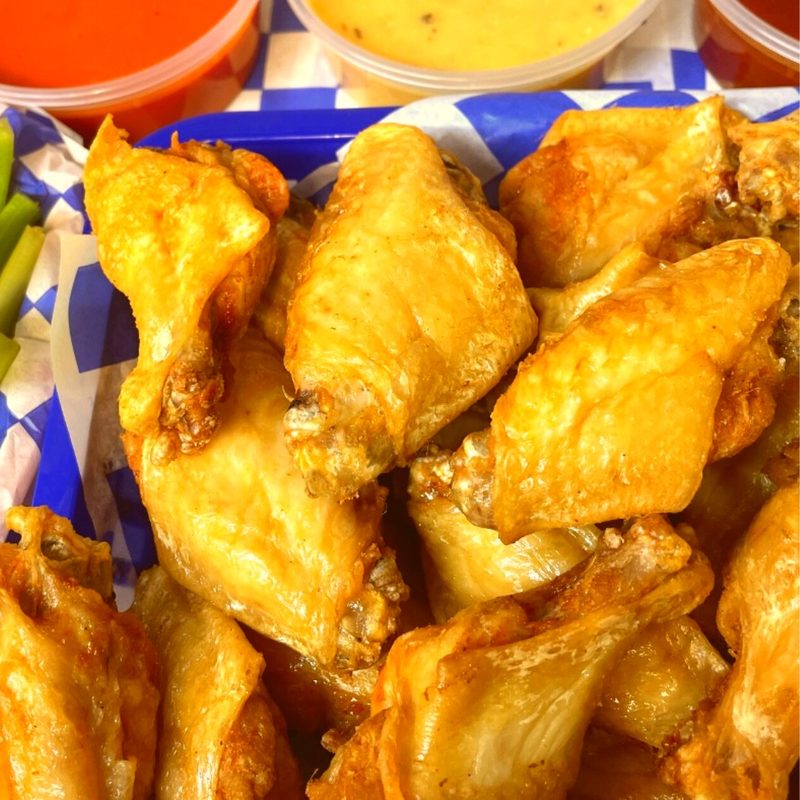 Basket of extra crispy golden wings with celery and dipping sauces